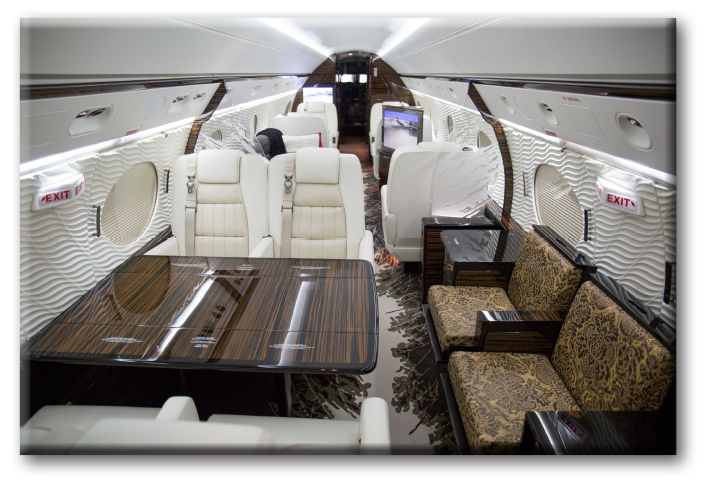 Interior of Corporate Wings’ Gulfstream 650 aircraft, highlighting white leather seats, modern wood finished table, sideways facing seats and glass privacy dividers.