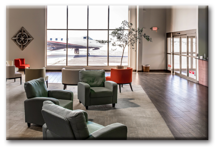 Corporate Wings FBO location featuring bespoke green, orange and beige luxury furniture and décor with a large cabin aircraft parked on tarmac outside of over-sized glass window